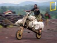 An image of a young man riding a wooden bike called a chukudu